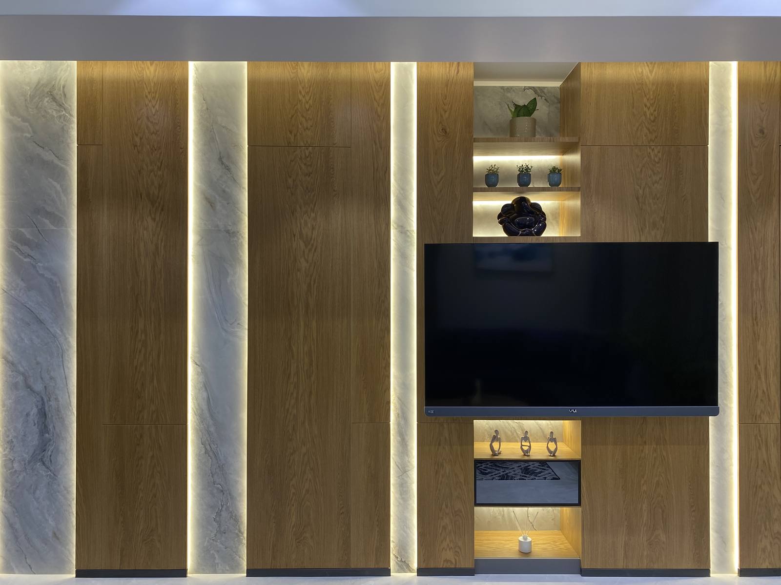 Marble-clad TV feature wall with backlit paneling by Beyond Briks